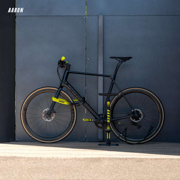 Schwarzes Fahrrad mit gelben AARON Fit Fahrradgriffen - Ergonomisch - Gelb an Lenker und Pedalen vor grauer Wand.
