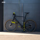 Schwarzes Fahrrad mit gelben AARON Fit Fahrradgriffen - Ergonomisch - Gelb an Lenker und Pedalen vor grauer Wand.