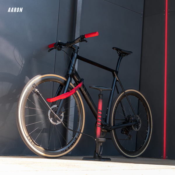 AARON Sport One Fahrradpumpe - Rot neben schwarzem Fahrrad mit roten Griffen und Pumpe an Wand stehend